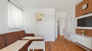 Una sala de estar moderna con un sofá marrón, una mesa de centro blanca, piso de madera, un televisor sobre una pared de madera y un cuadro en la pared.