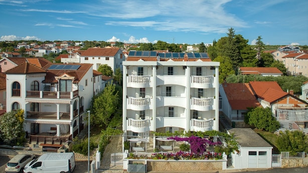 Un edificio de varios pisos con balcones, paneles solares en el techo y un jardín con flores moradas.