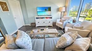 Ett vardagsrum med en soffa, fåtöljer, ett soffbord, en tv och utsikt över en stadssiluett genom stora fönster.