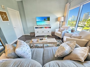 Een woonkamer met een bank, fauteuils, een salontafel, een televisie en een uitzicht op een stadsbeeld door grote ramen.