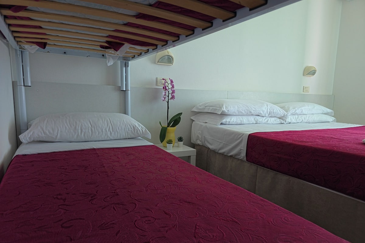 Una habitación con dos camas, cada una con cubrecama rojo, almohadas blancas y una pequeña planta en maceta en la mesita de noche.
