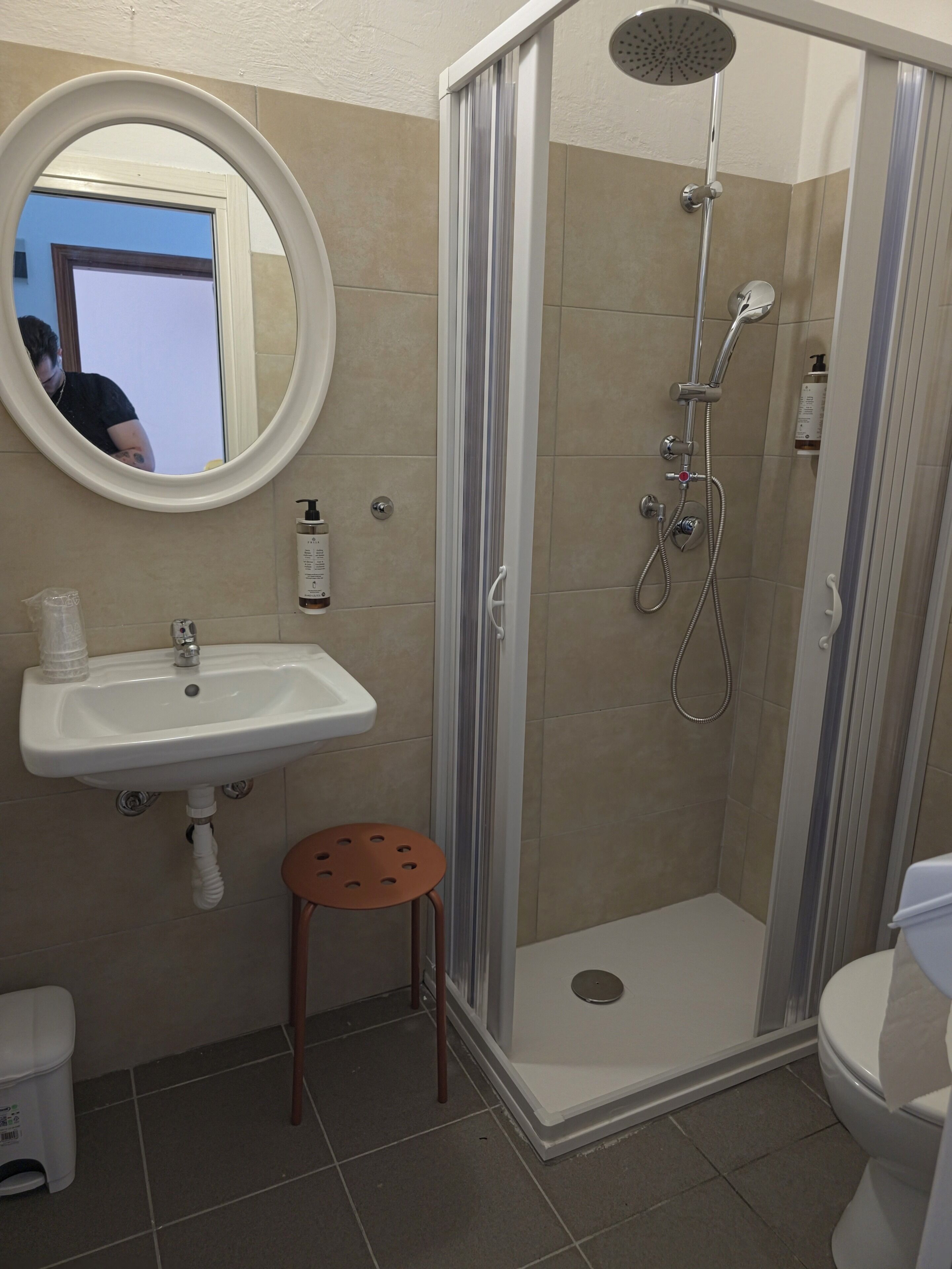 Une salle de bain équipée d’une douche, d’un lavabo, de toilettes et d’un petit tabouret.