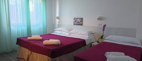 A hotel room with two beds, a window with curtains, an air conditioning unit, a clock, and a small potted orchid.