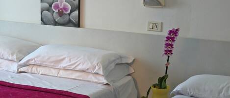 A hotel room with two beds, a nightstand with a lamp, a wall-mounted switch, and a framed picture of an orchid.