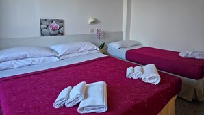A hotel room with two beds, each with white linens and a red bedspread. There are towels on the beds and a wall-mounted light fixture. - Hotel Ornella (Bellaria-Igea Marina)