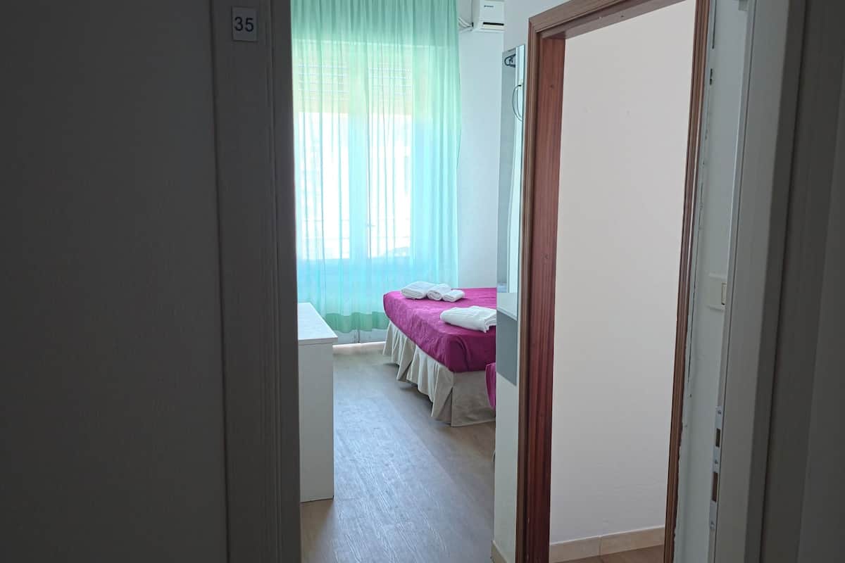Una habitación con cama, ventana con cortinas y puerta.