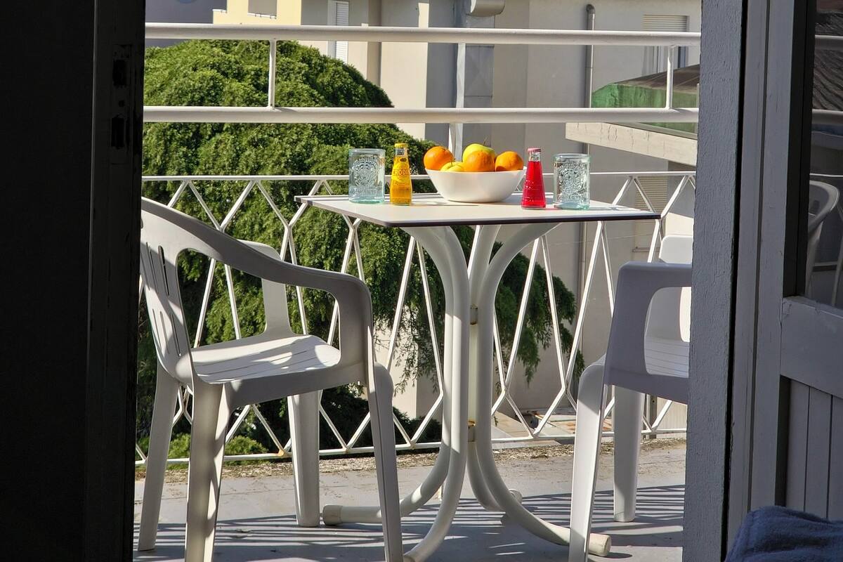 Un balcón con una mesa, sillas y un cuenco de fruta.