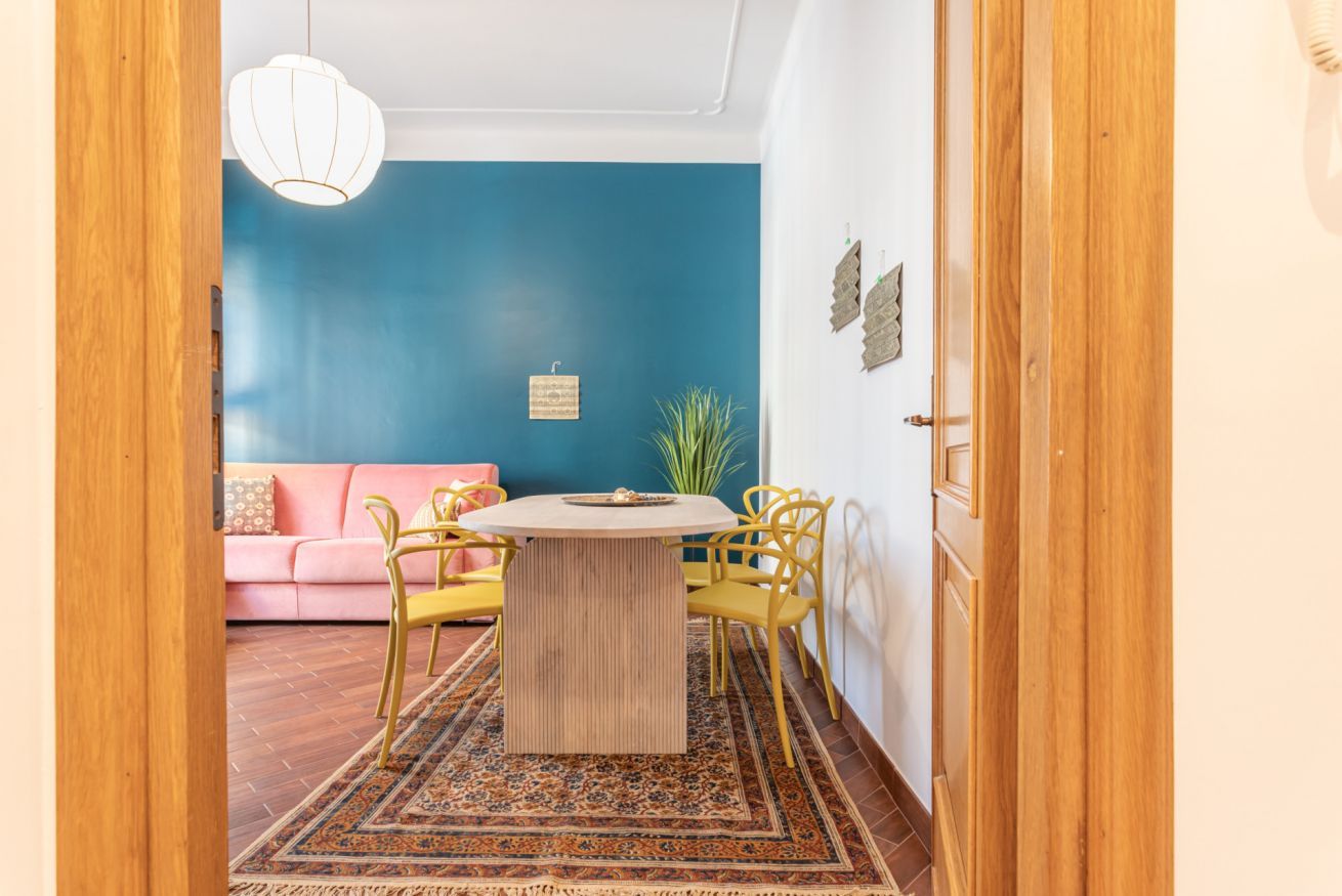 A room with a round table, yellow chairs, a pink sofa, and a blue accent wall.