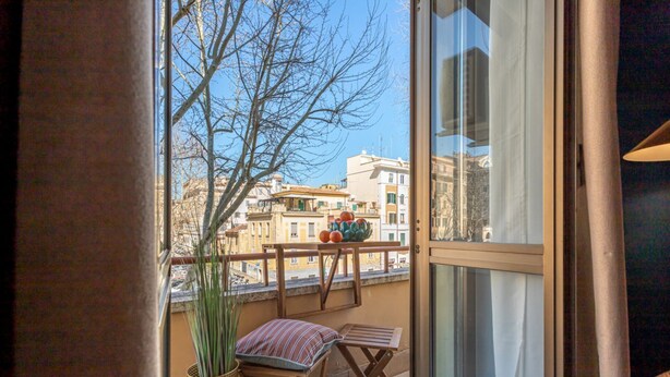 Ein Balkon mit Blick auf Gebäude, einem Blumentopf und einem gestreiften Kissen.