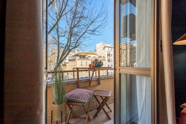Ein Balkon mit Blick auf Gebäude, einem Blumentopf und einem gestreiften Kissen.