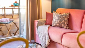 Ein gemütlicher Wohnbereich mit einem rosafarbenen Sofa, gemusterten Kissen und einer Stehlampe.