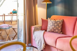Ein gemütlicher Wohnbereich mit einem rosafarbenen Sofa, gemusterten Kissen und einer Stehlampe.