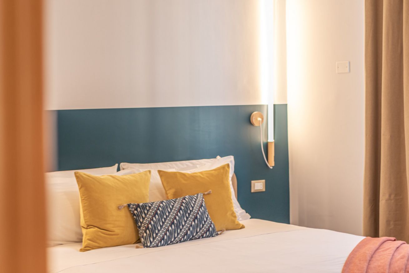 A neatly made bed with white and yellow pillows, a blue headboard, and a bedside lamp.