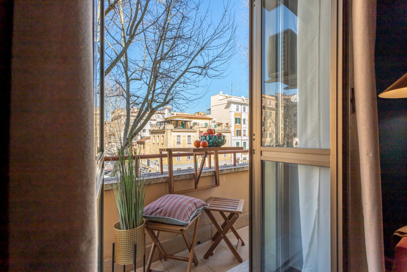 A balcony with a view of buildings, a potted plant, and a striped cushion.