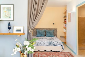 Une chambre à coucher avec un lit, un rideau, une étagère remplie de livres et un vase avec des fleurs.