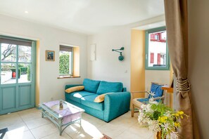 Un salon avec un canapé de couleur turquoise, une petite table, un fauteuil et une fenêtre donnant sur des immeubles.