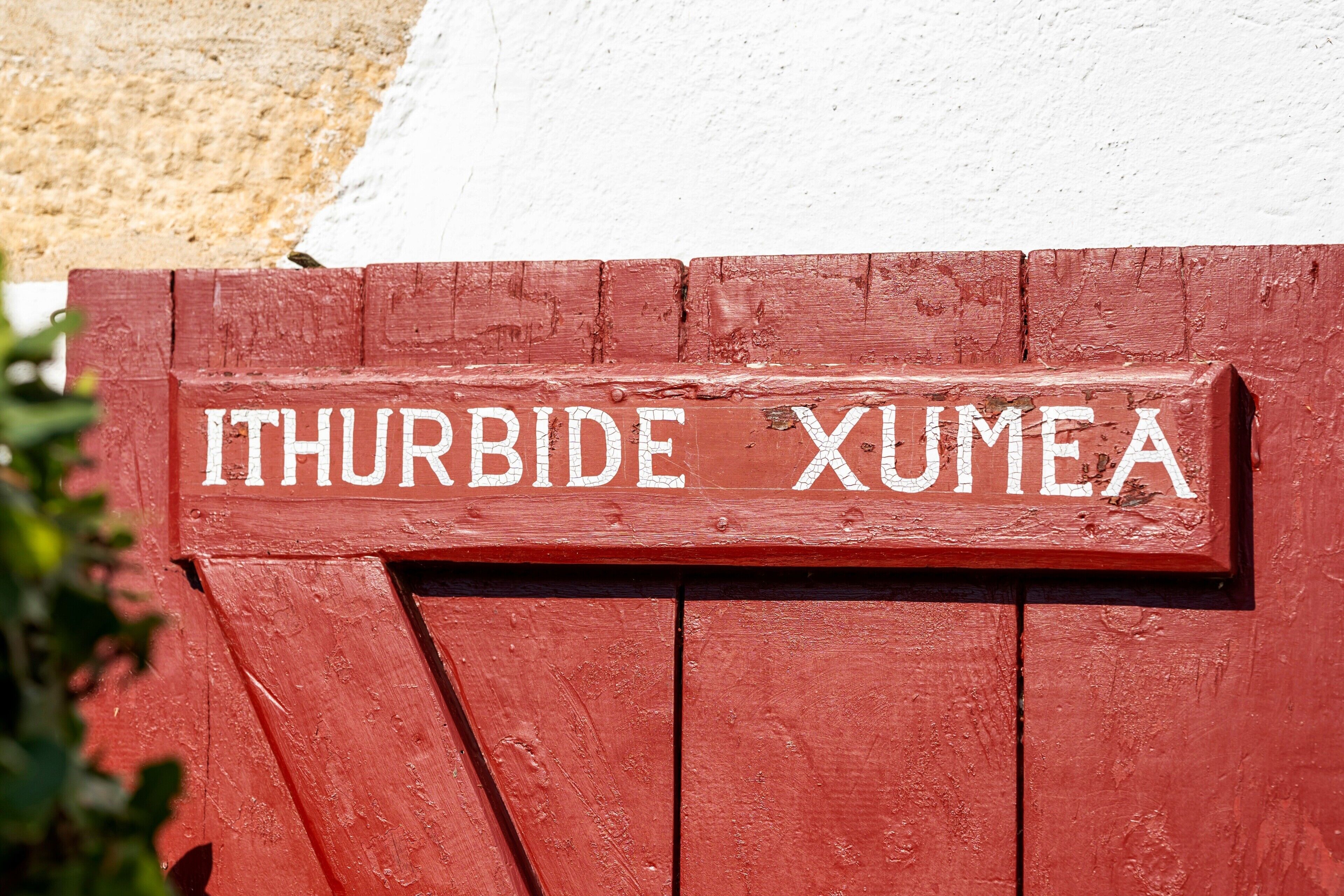 A red wooden sign with white lettering that reads 'ITHURBIDE XUMEA'.