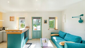 Un salon moderne avec un canapé de couleur turquoise, une table basse et un coin cuisine doté d’un comptoir et de placards.