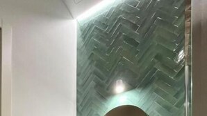 A modern bathroom with a herringbone-patterned wall, a round mirror, a wooden vanity, and a white sink. - suite la pennichella (Agropoli)