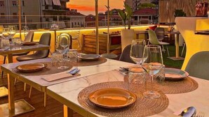 A rooftop dining area with tables set for two, large umbrellas, and a cityscape view at sunset. - suite la pennichella (Agropoli)
