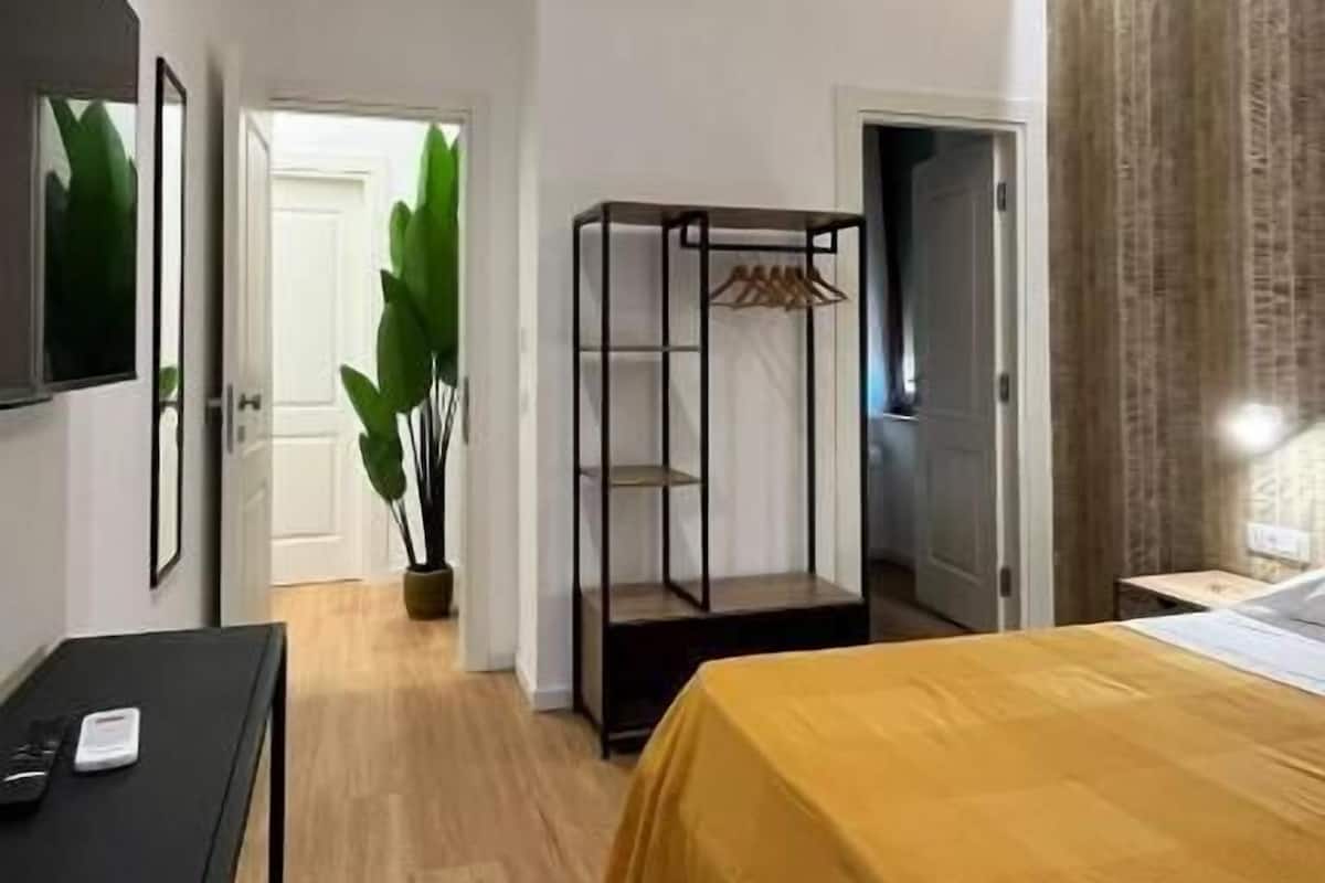 A bedroom with a bed, a desk, a wardrobe, and a plant.