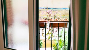 A view through a window with a metal railing, potted plants, and a glimpse of a building exterior. - Colosseum: Entire Guest House (2BR en-suite/2BA) (Roma)