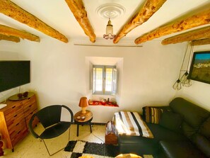 Un accogliente soggiorno con travi a vista in legno, una televisione, un divano, una poltrona e un tavolino con una lampada.