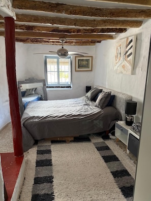 Una camera da letto con un letto, una finestra, una ventola a soffitto e un quadro appeso al muro.