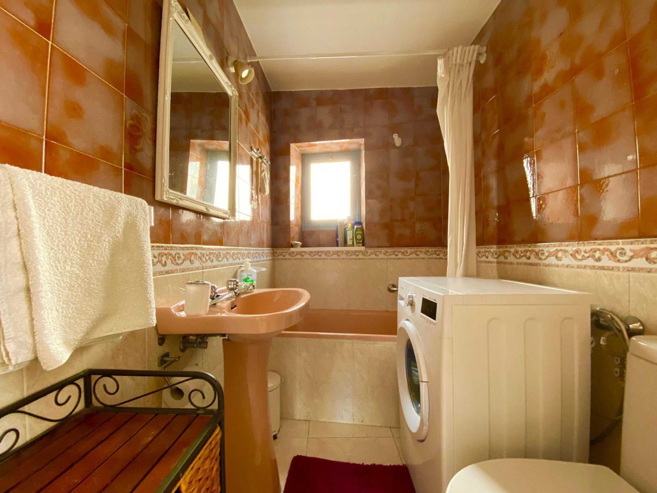A bathroom with a sink, mirror, window, shower, and a washing machine.