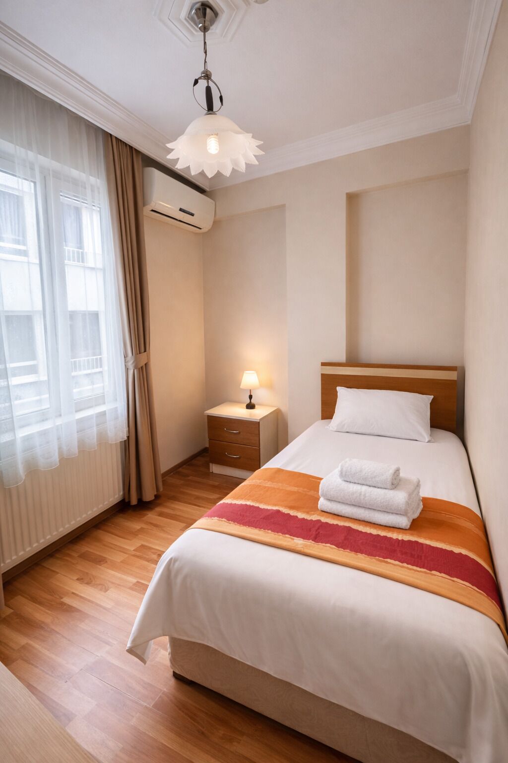 Et hotelværelse med seng, natbord, lampe og et vindue med gardiner.