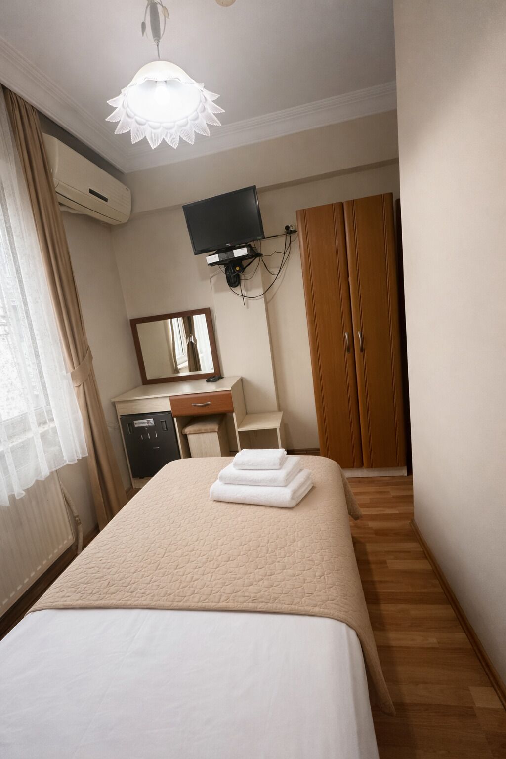 A hotel room with a bed, a desk, a television, a wardrobe, and a mirror.