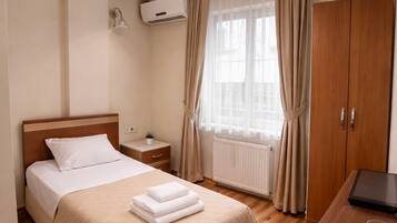 Habitación de hotel con cama, mesita de noche, lámpara, ventana con cortinas y escritorio con computadora portátil.