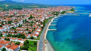 Vista aérea de una ciudad costera con edificios de techo rojo muy juntos a lo largo de la costa, un mar azul claro y un paisaje montañoso al fondo.
