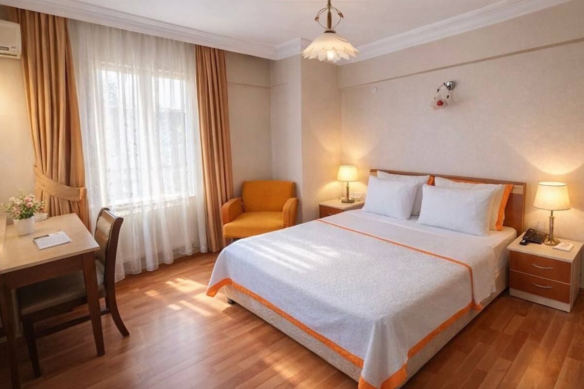 A hotel room with a large bed, a desk with a chair, a nightstand, and a lamp.