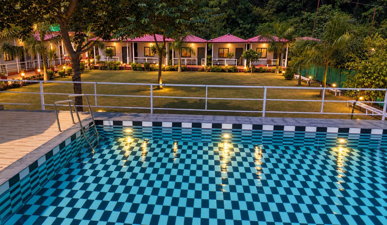 A swimming pool with a checkered pattern, surrounded by a deck and a fence.