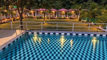 A swimming pool with a checkered pattern, surrounded by a deck and a fence.