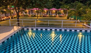 A swimming pool with a checkered pattern, surrounded by a deck and a fence.