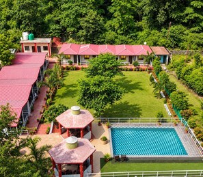 A hotel with multiple red-roofed buildings, a swimming pool, and a well-maintained lawn. - Ekantam Riverside Resort (Rishikesh)
