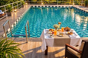 A poolside dining area with a table set for breakfast, surrounded by a pool with checkered tiles. - Ekantam Riverside Resort (Rishikesh)