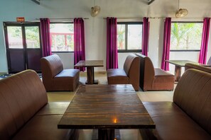 Un espace repas avec des banquettes en cuir marron, une table centrale et des fenêtres ornées de rideaux violets.