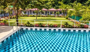 Una piscina con diseño de cuadros, rodeada por un césped cuidado y una hilera de edificios con tejados rojos.
