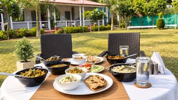 Una mesa de comedor al aire libre con diversos platos, un vaso de agua y una pequeña planta en maceta.