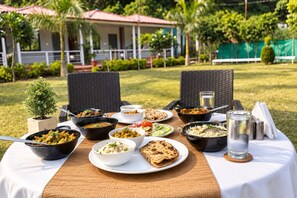 Una mesa de comedor al aire libre con diversos platos, un vaso de agua y una pequeña planta en maceta.