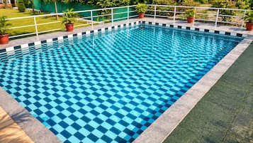 Piscina rectangular con diseño ajedrezado, rodeada por una baranda blanca y macetas con plantas.