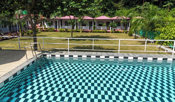 A swimming pool with a checkered pattern, surrounded by a white fence, with a building in the background.