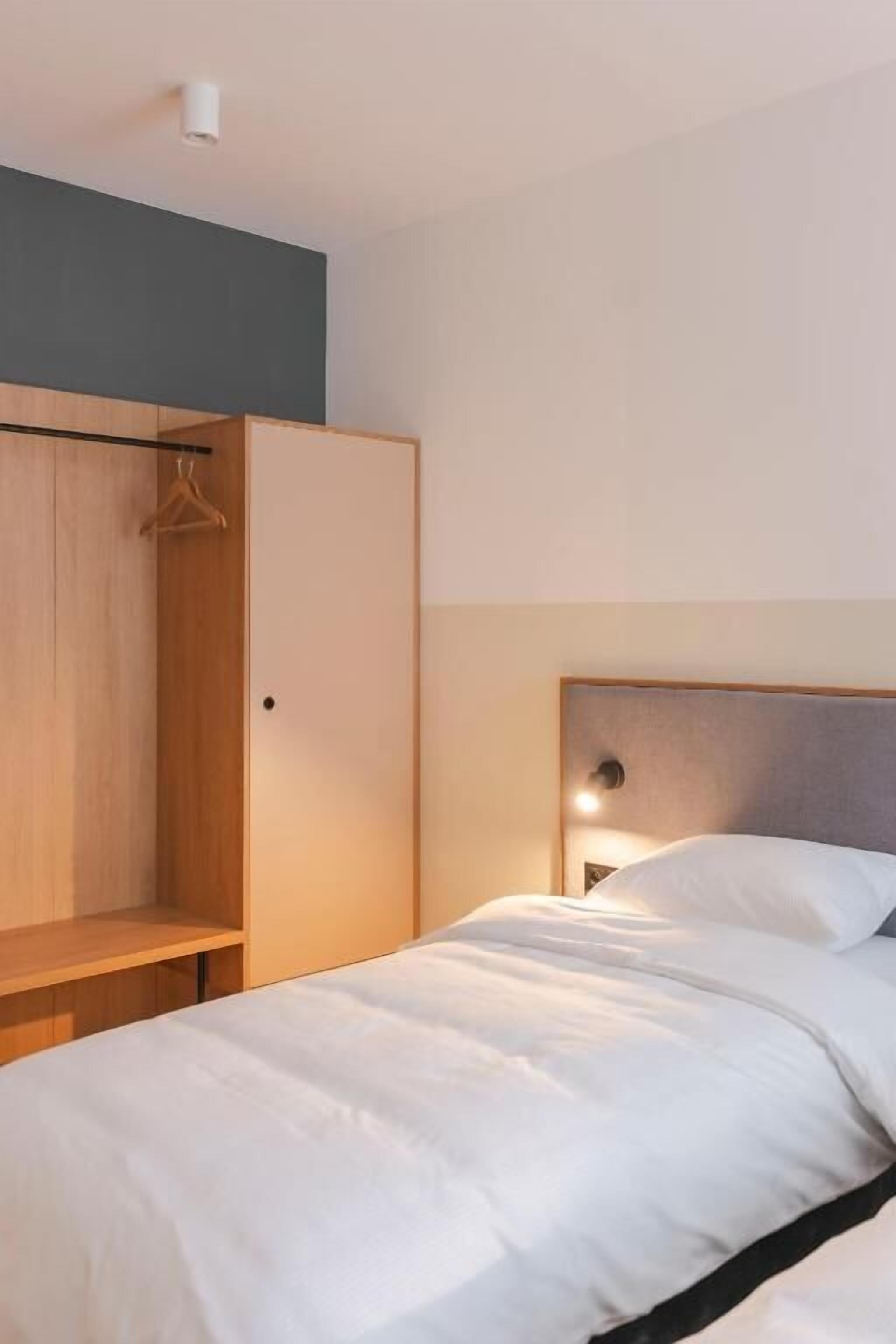 A hotel room with a bed, a wooden wardrobe, and a nightstand.