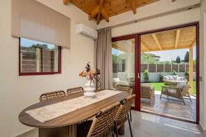 A dining area with a wooden table, wicker chairs, a vase with flowers, and a view of a garden through a glass door.