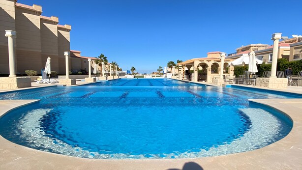 A large, clear swimming pool with a curved edge, surrounded by a beige tiled deck. - Arena Beach Resort (Hurghada)