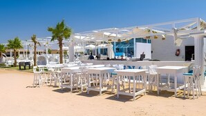A beachside restaurant with white tables and chairs, a covered seating area, and a view of the sea. - Arena Beach Resort (Hurghada)