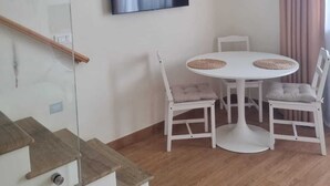 Ein modernes Wohnzimmer mit einem an der Wand befestigten Flachbildfernseher, einem runden weißen Tisch mit zwei Stühlen und einer Treppe mit Glastrennwand.